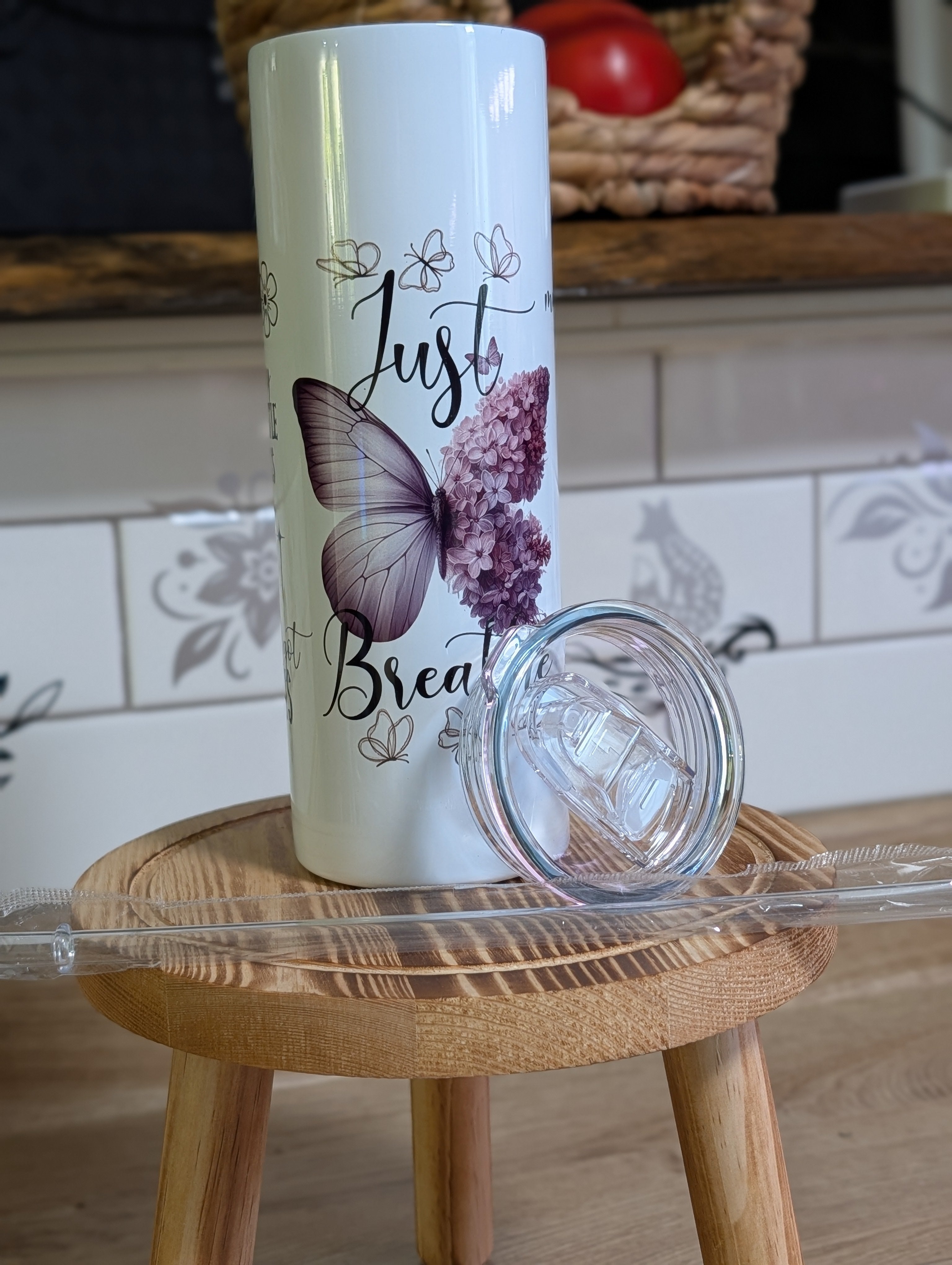 Just Breathe butterfly tumbler with lid off on wooden stool showing butterfly and hydrangea design