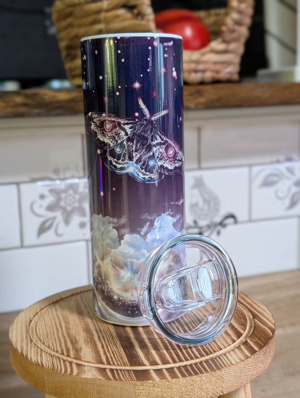 Celestial moth night sky tumbler front view with lid off on wooden stool