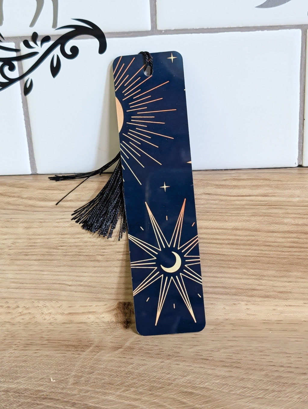 Celestial bookmark front - navy background with crescent moon, gold sunburst and stars with black tassel