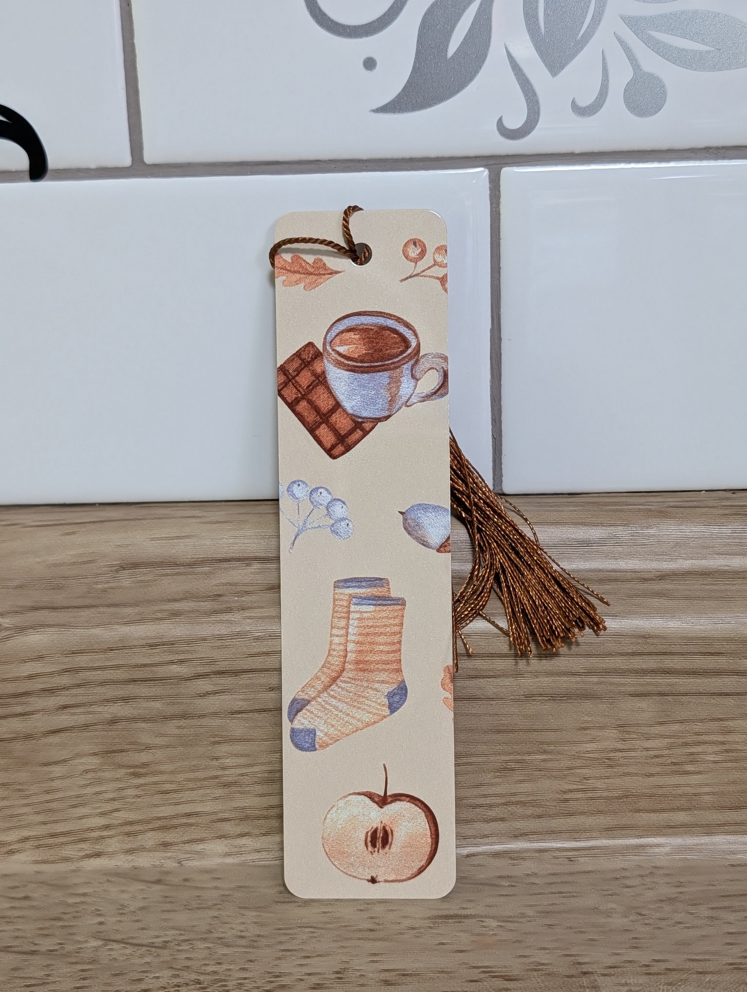 Cozy autumn bookmark back - cream background with hot cocoa, chocolate, cozy socks, acorns and apple with bronze tassel