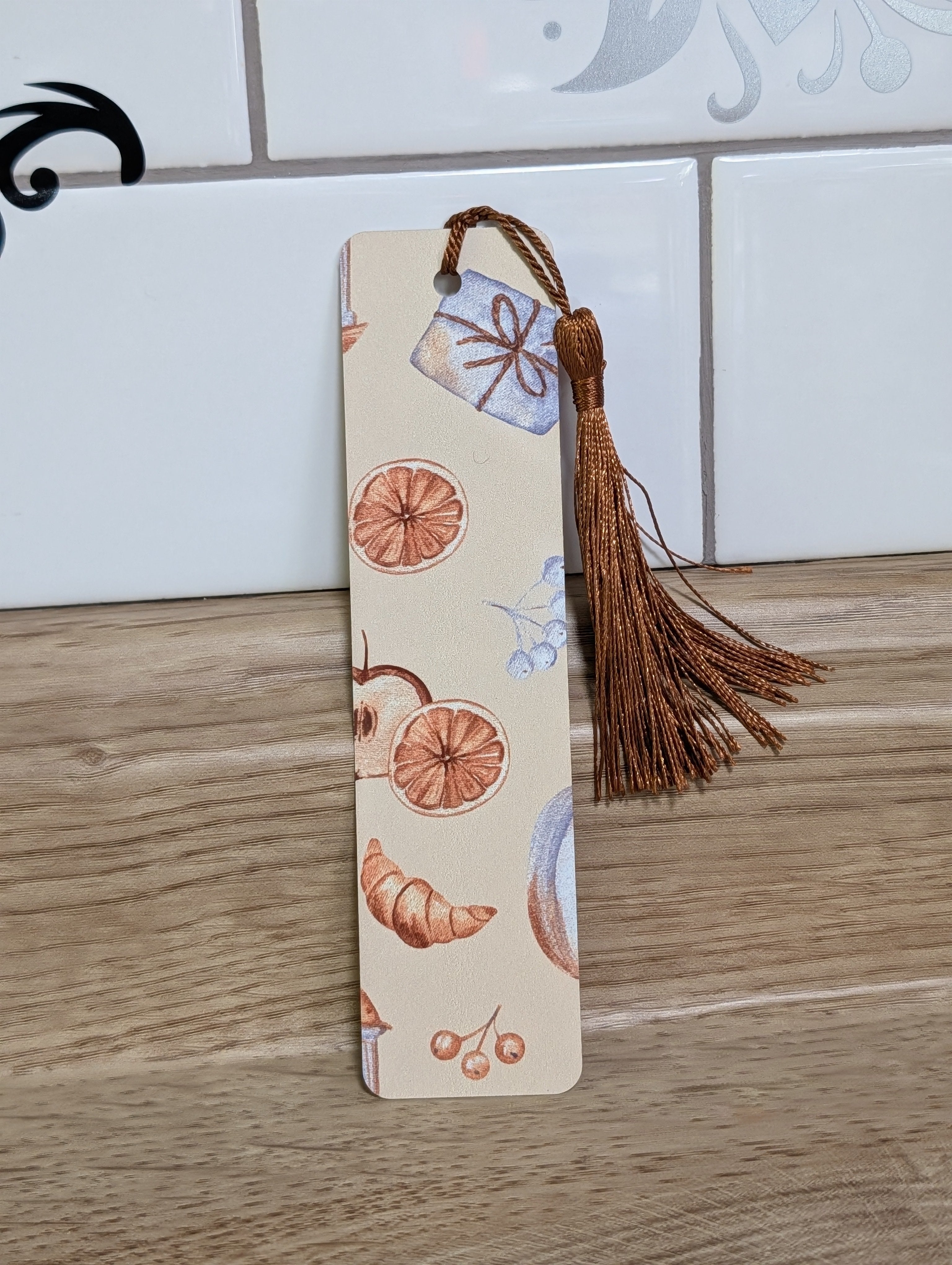 Cozy autumn bookmark front - cream background with dried oranges, croissant, cherries and gift box with bronze tassel