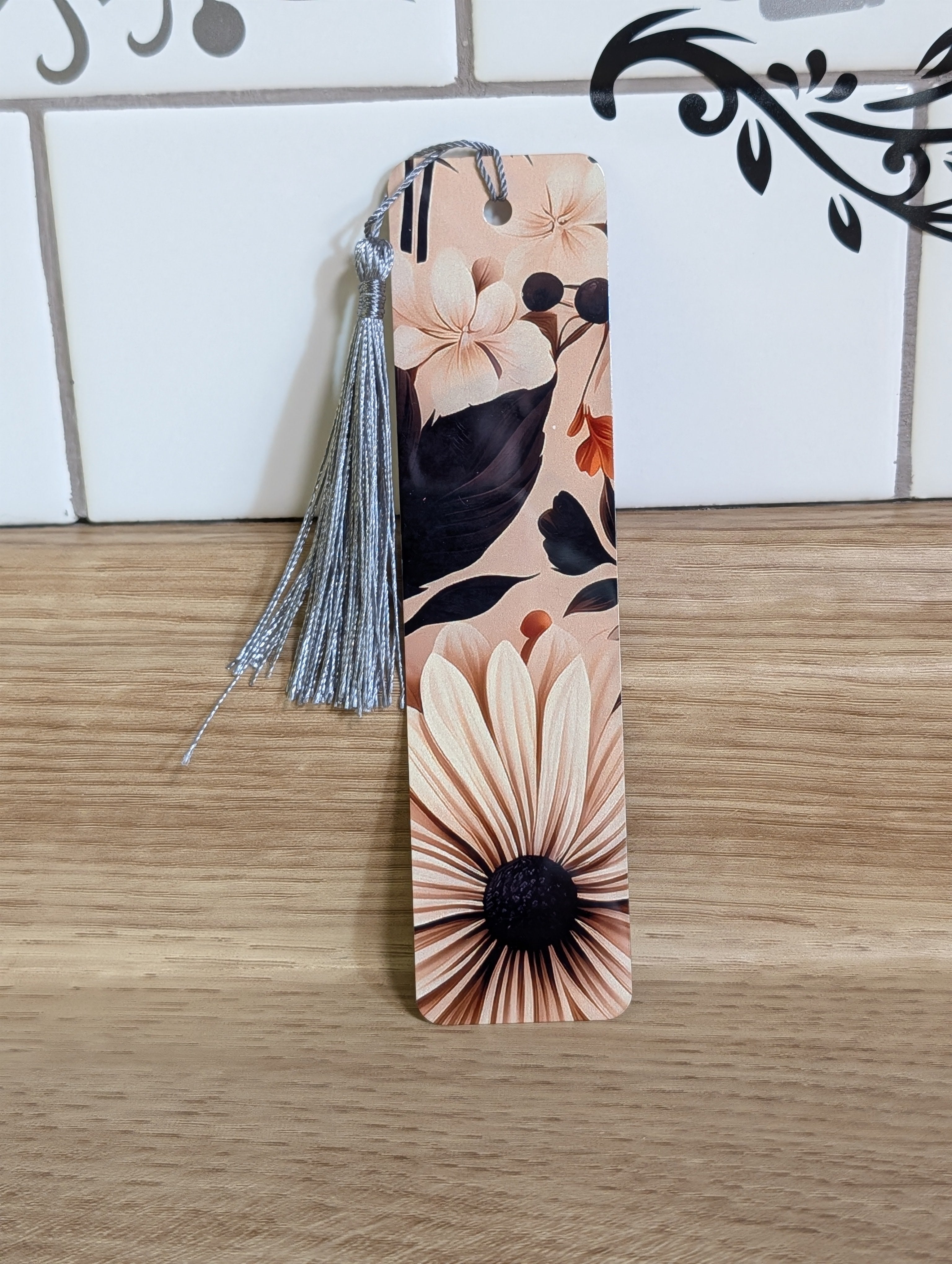Dark floral bookmark front - blush background with white daisy, rust orange blooms and dark botanical leaves with silver tassel