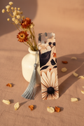 Dark Floral Bookmark with silver tassel standing upright against cream ceramic vase with dried rust and cream wildflower stems on warm blush linen with scattered petals