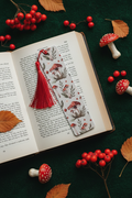 Mushroom Bookmark with red tassel tucked into open hardcover book on mossy green surface with real small mushrooms dried leaves and red berries