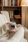 Woman in cream knit sweater holding Easily Distracted By Cats and Books Coffee Mug curled in armchair reading nook with bookshelf and black cat nearby